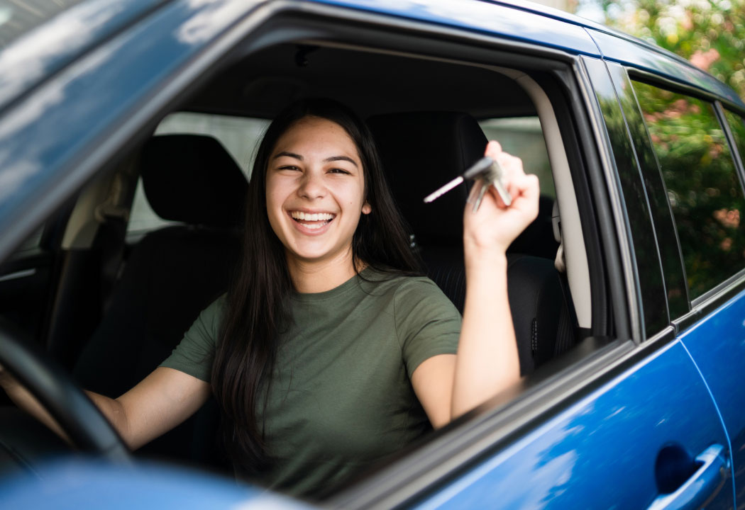 young woman sitting in a car holding up a pair of car keys